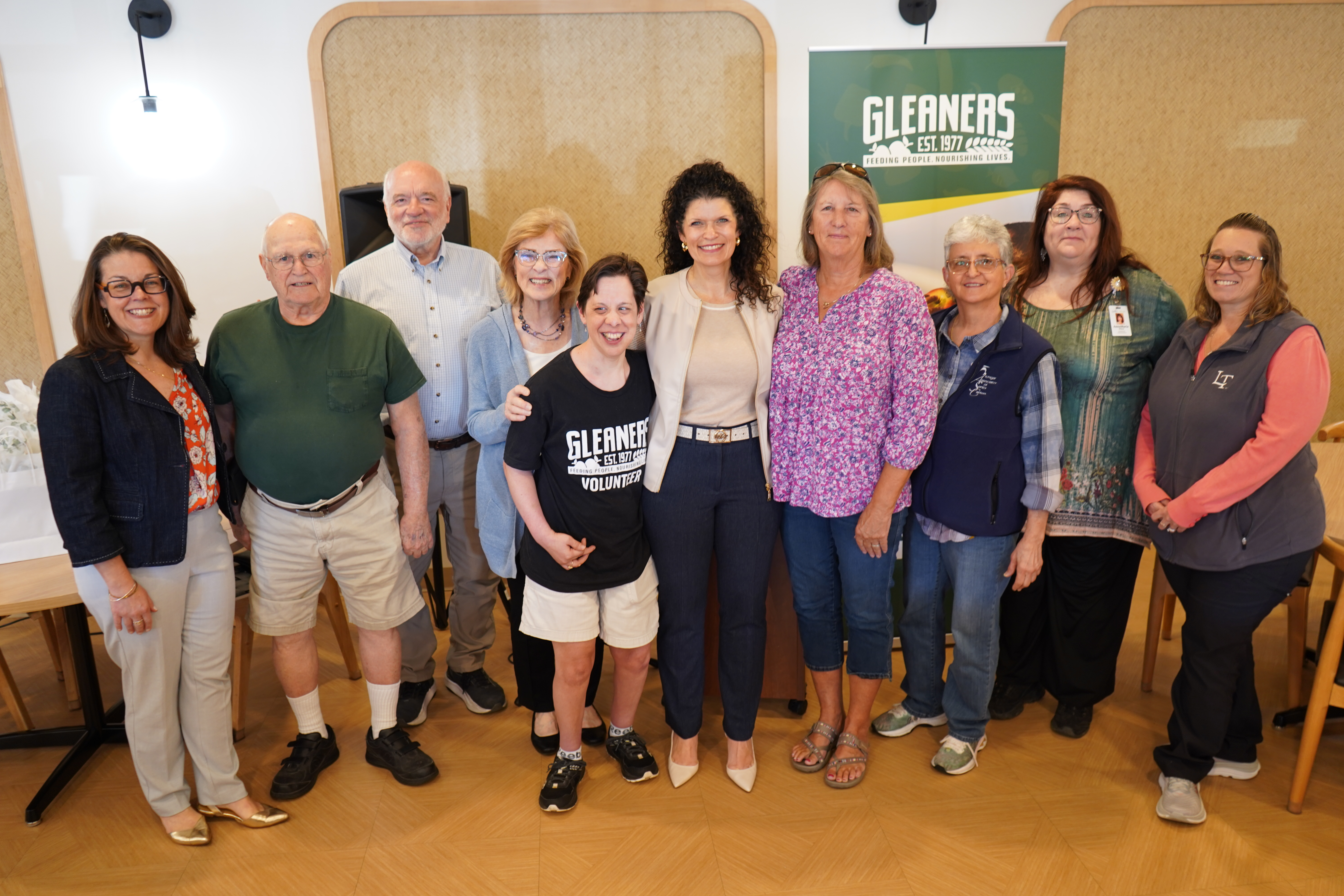 Group of ten adults posing for a photo indoors in front of a GLEANERS banner, smiling and standing together for a community event.