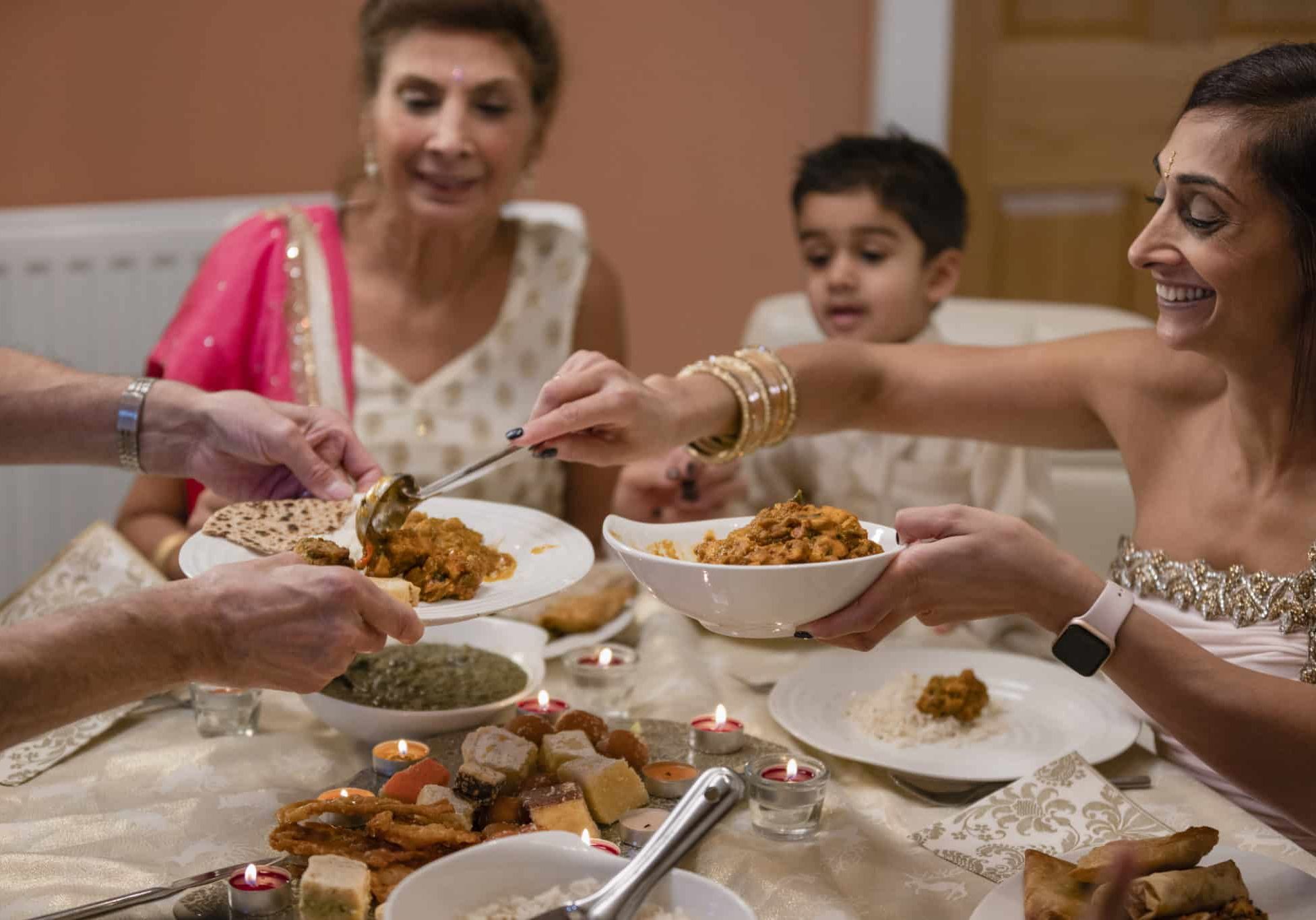 A medium close up of a woman serving an unrecognisable family member some curry that has freshly been made onto their plate. They are celebrating Diwali in her family home in the North East odf England.